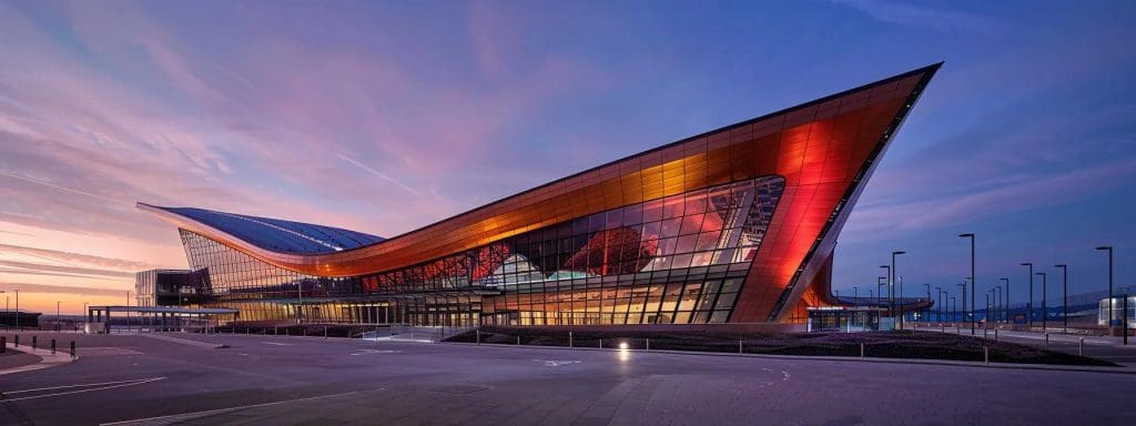 a sleek, modern architectural façade of the cardiff international sports village showcases sharp geometric lines, expansive glass surfaces, and the innovative integration of sustainable materials, embodying the principles of functional innovation and aesthetic minimalism under bright artificial lighting.